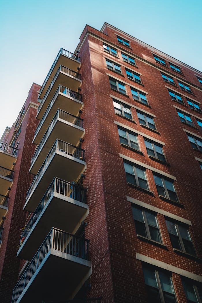 A tall brick apartment building with balconies in urban sunlight.